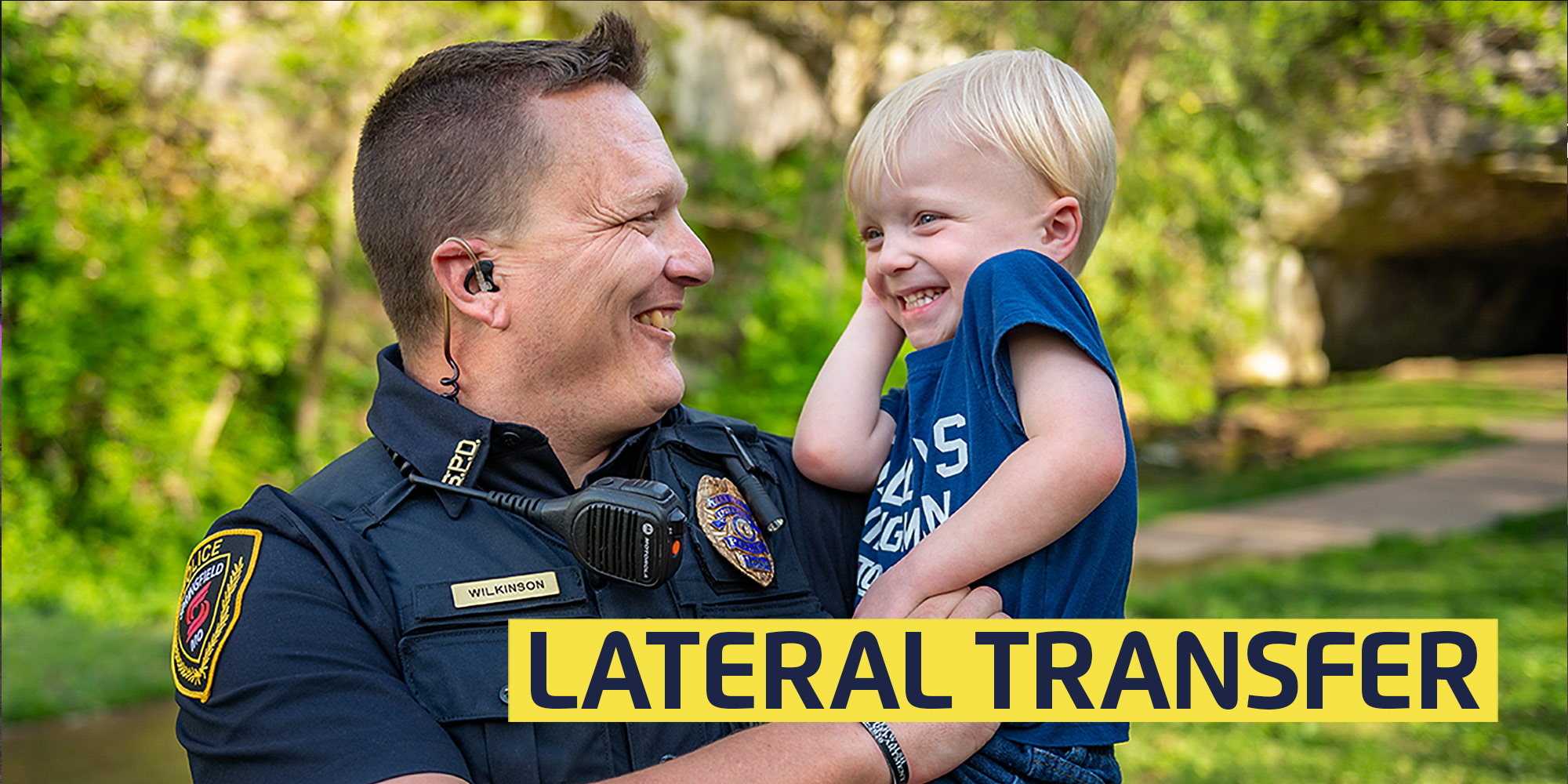 smiling police officer holding laughing son in a park with text: lateral transfer