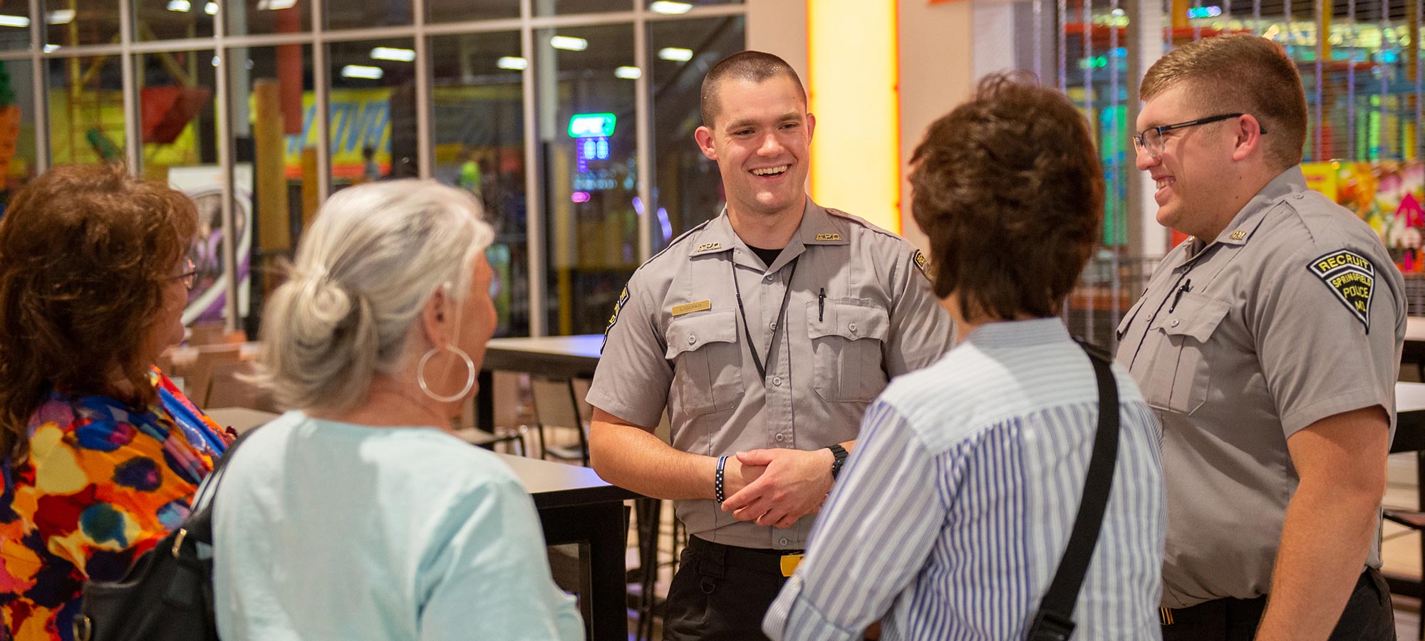 two police recruits smiling and talking with citizens in a mall
